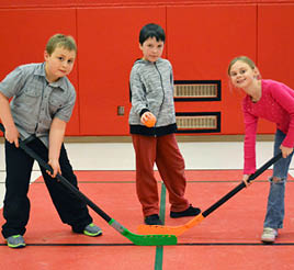Two children hold hockey sticks, while another hold a ball as they begin floor hockey.
