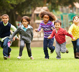 A group of diverse children wearing sweaters run on the grass.