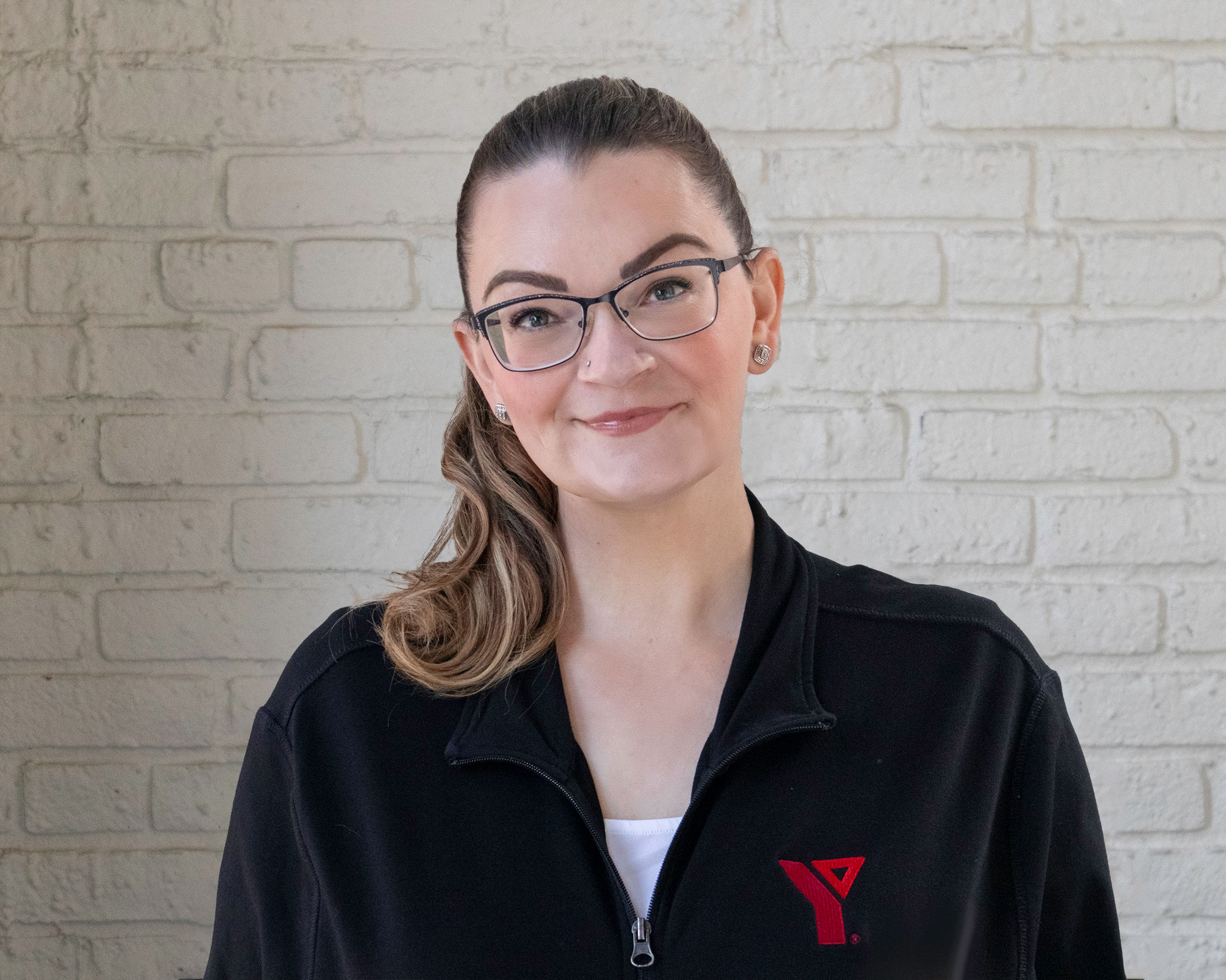 A young, professional woman, Laura Svajlenko, wearing glasses and a YMCA uniform smiles.