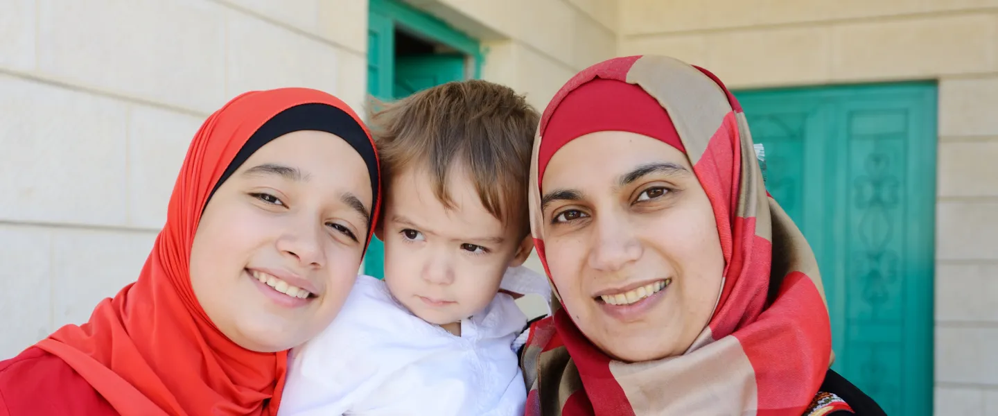 A teenage girl, young boy and their mother stand on their front porch, posing for a photo.