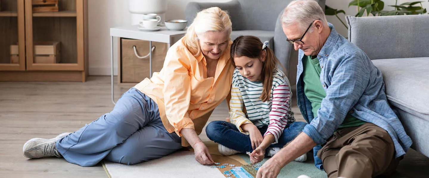 A grandmother, granddaughter and grandfather put a puzzle together on their livingroom floor.