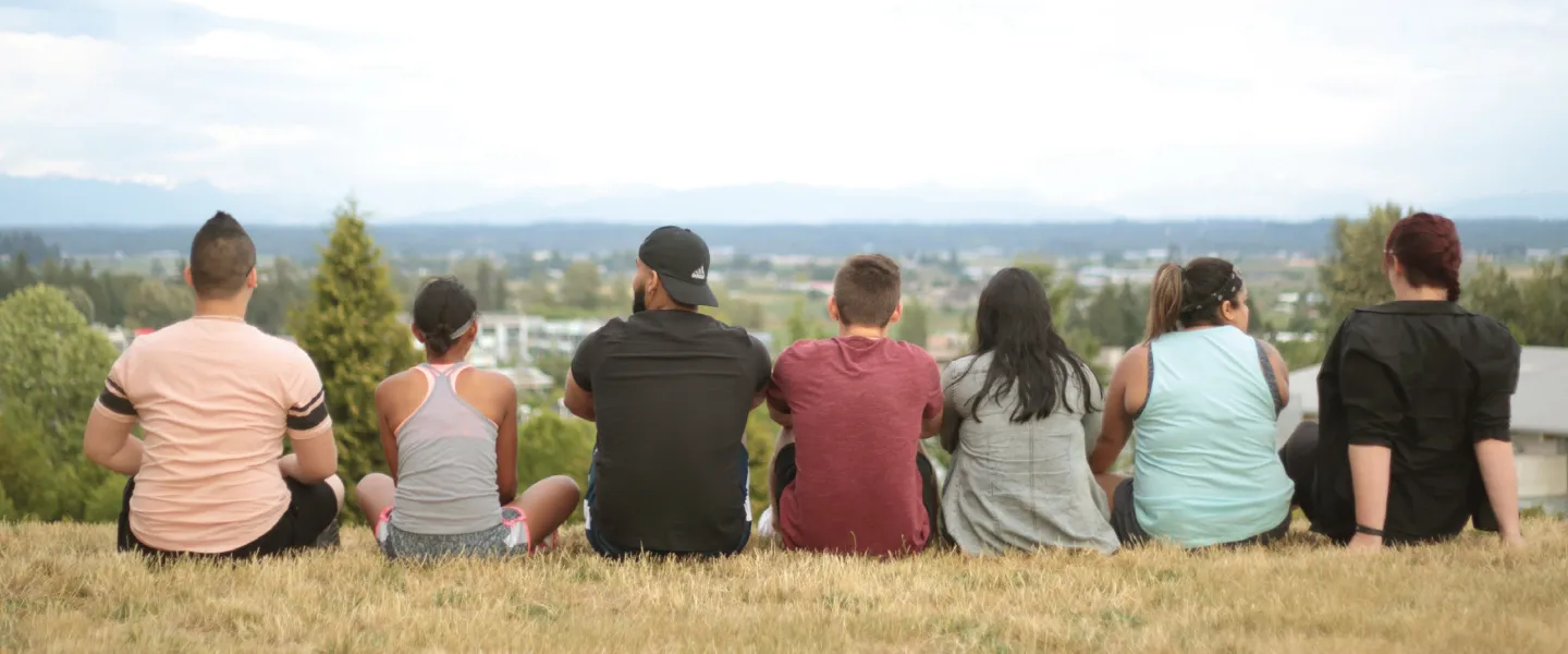 A group of teens and program facilitators sitting on top of a hill, overlooking a city.