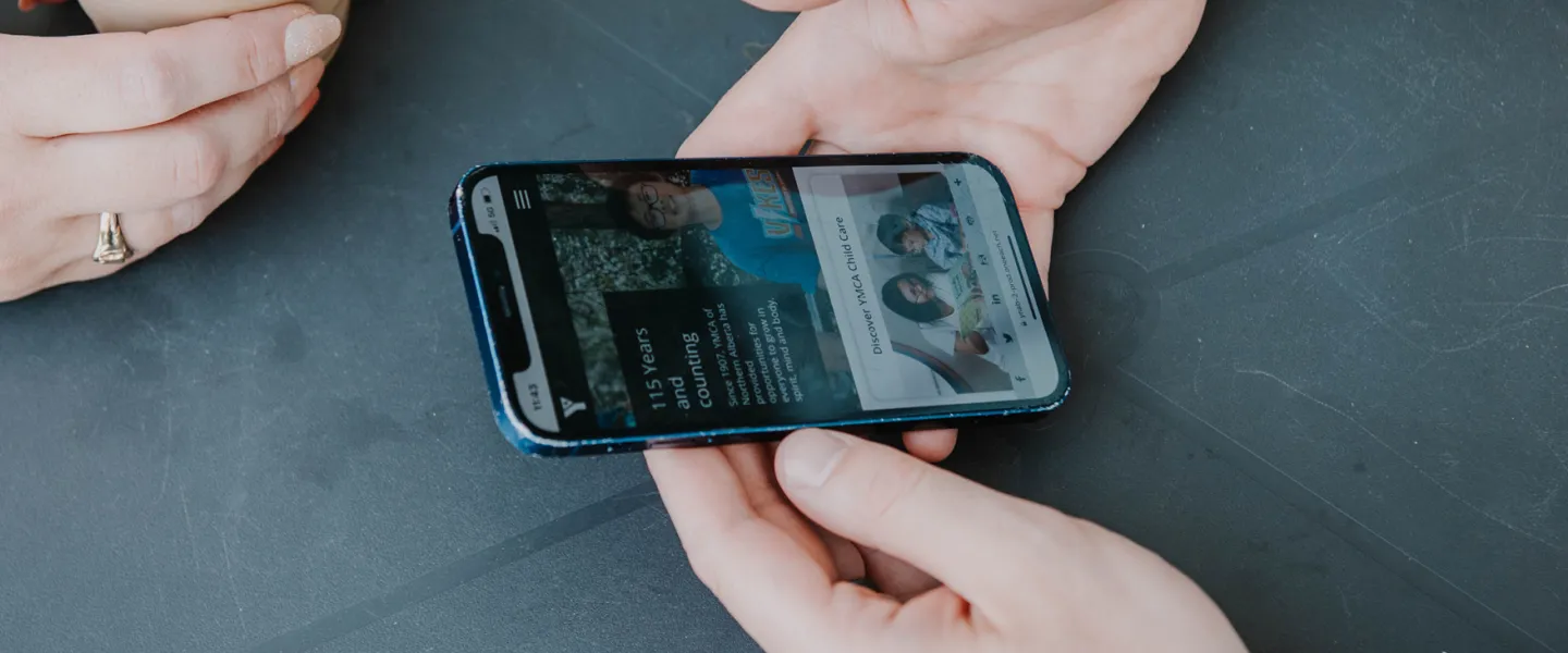 a person holding a phone browsing YMCA website
