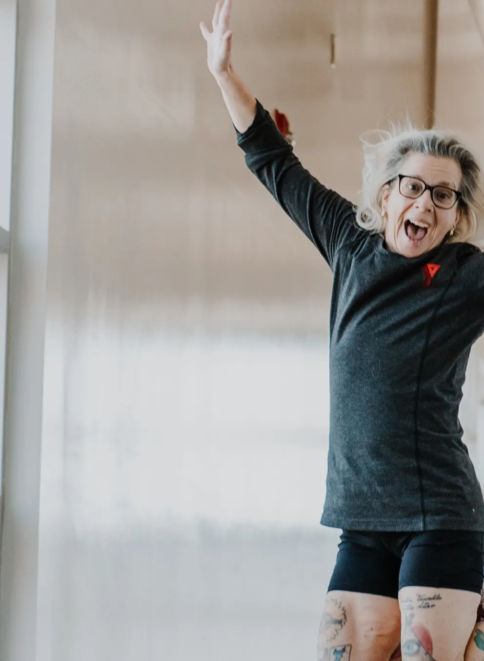 A young woman wearing a grey long-sleved shirt seen with a YMCA logo jumps in the air while on an indoor walking track.