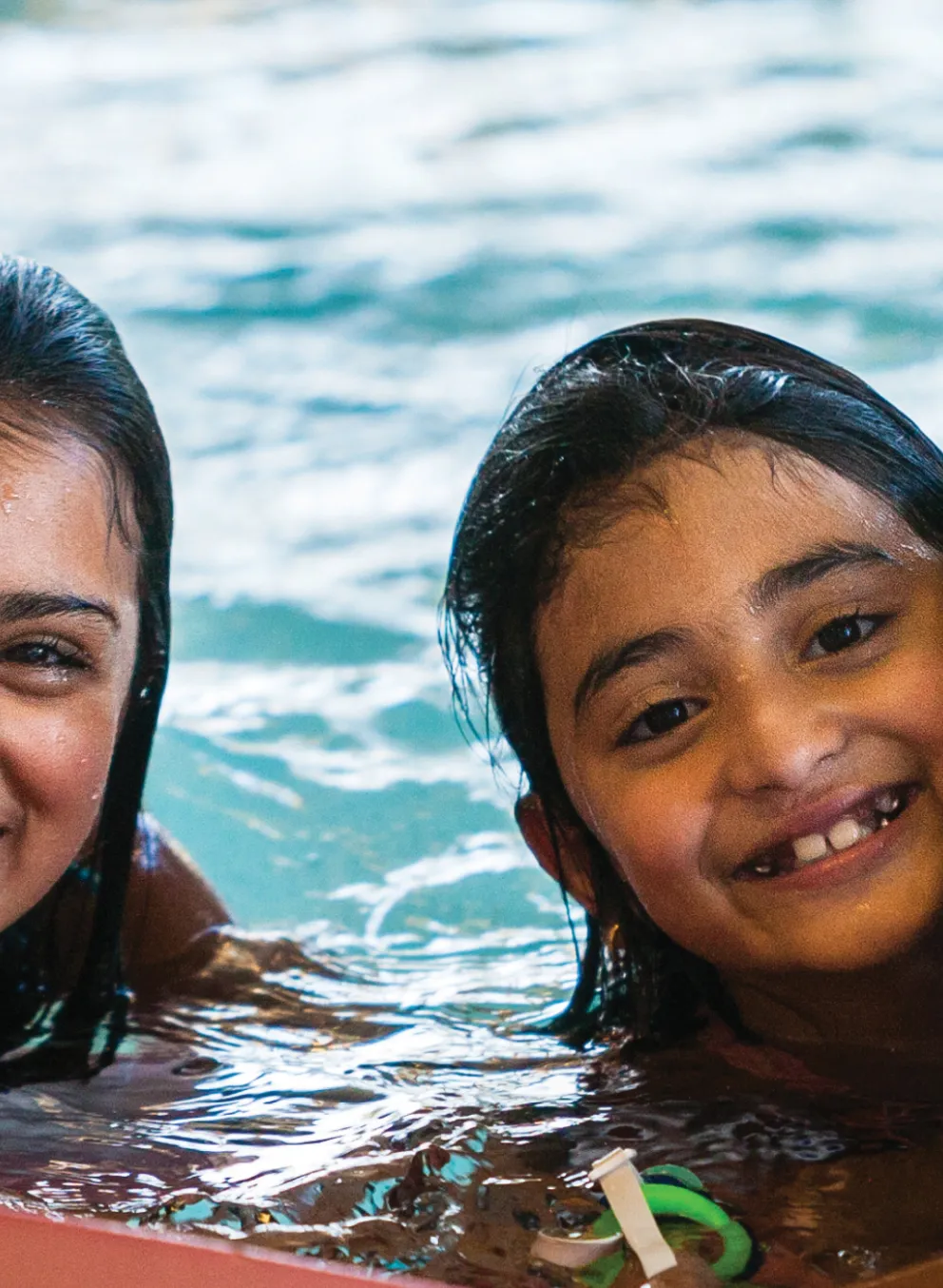 Three kids in a pool hold onto a toy and pose for a photo.