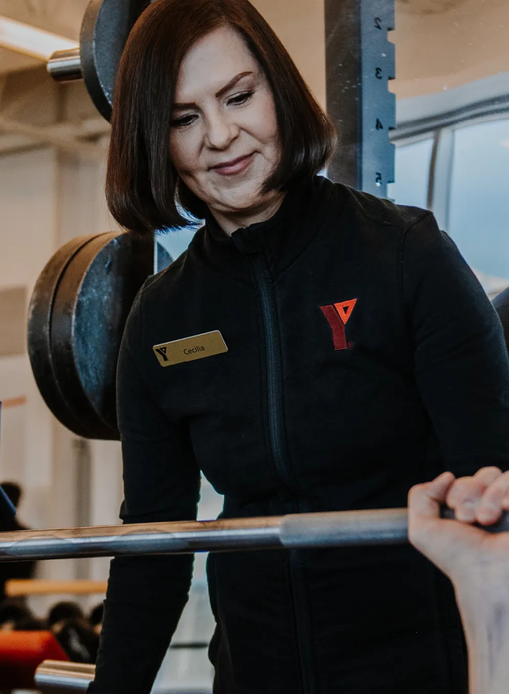 A female personal trainer stands behind a male member as he uses a barbell bench press.