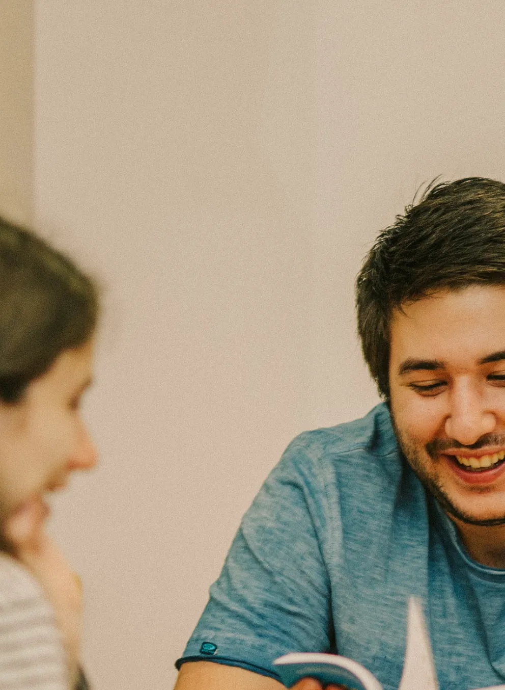 A teenage girl, teenage boy and male youth leader sit at a table reading a book together.