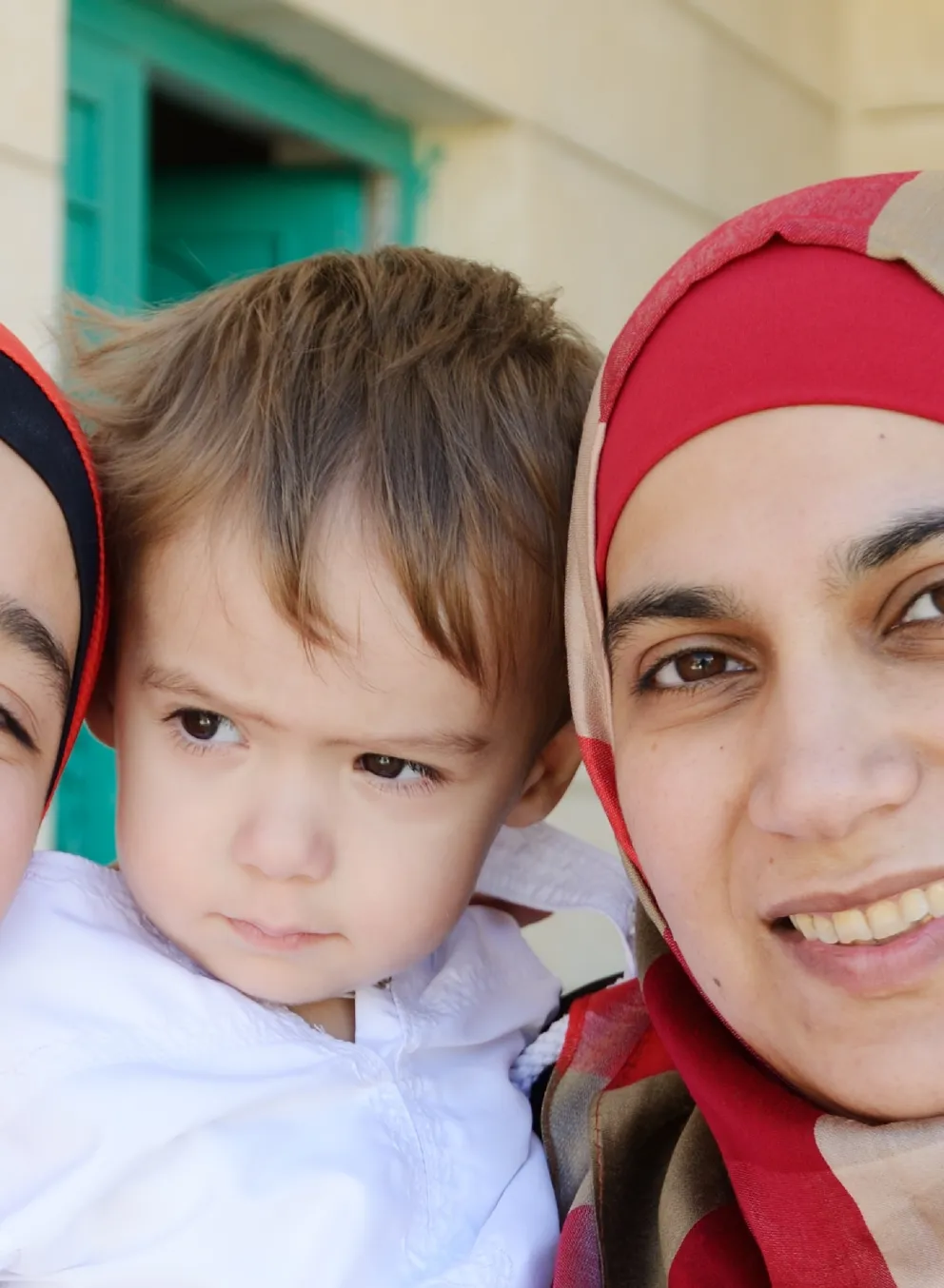 A teenage girl, young boy and their mother stand on their front porch, posing for a photo.