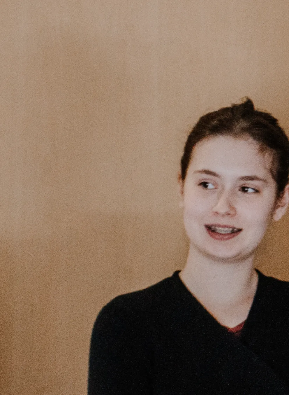 Two teenage girls stand infront of a classroom and listen to one of their peers talking.