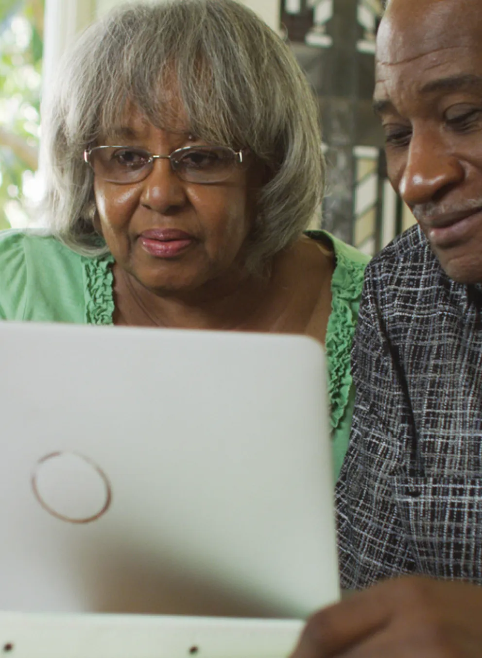 An older man and woman sit close together, using a computer at dinning room table.
