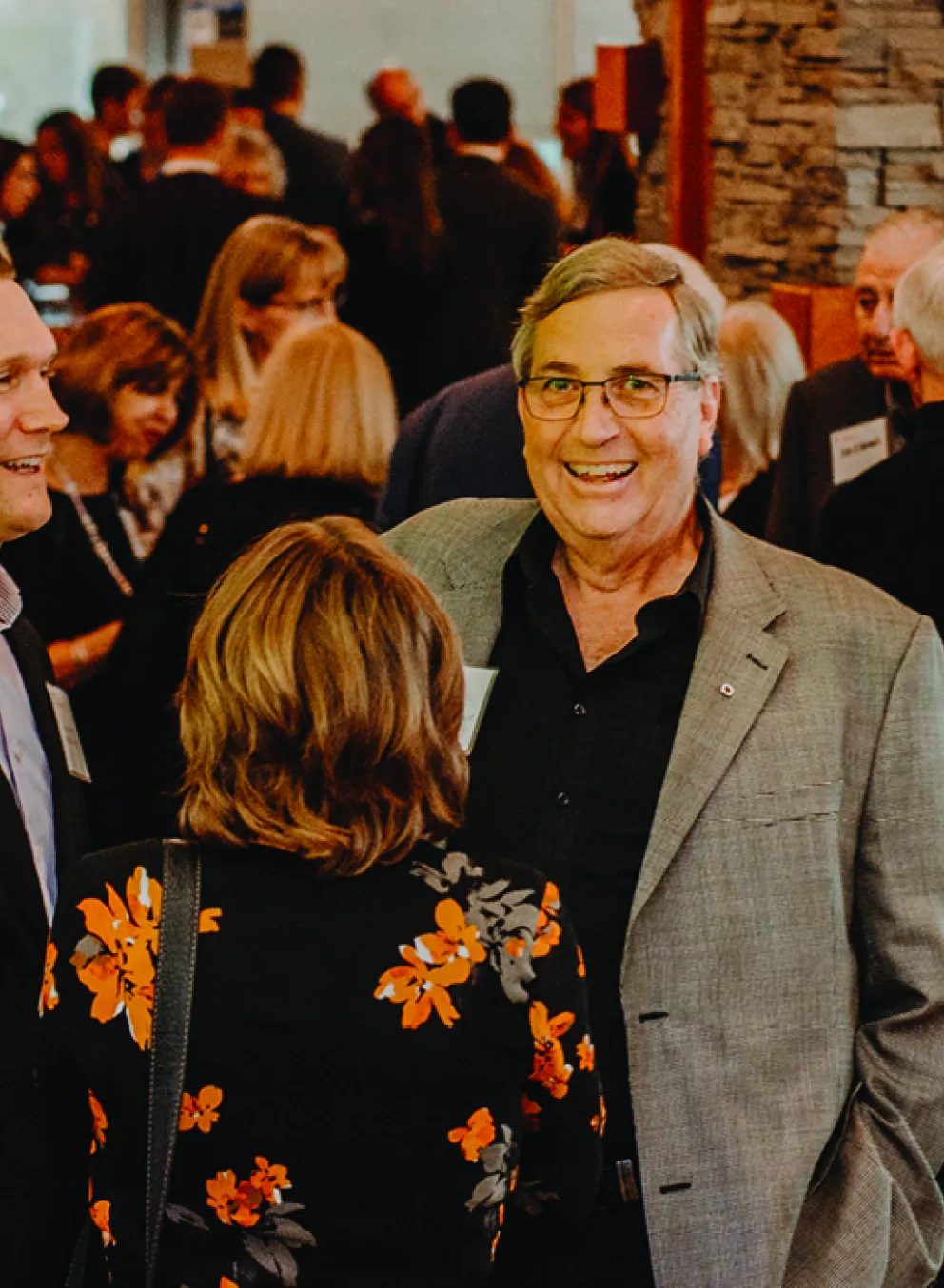 An older man in a suit shares a laugh in a diverse room of people while at a fundraising event.