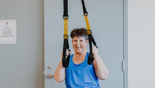 An older women wearing athleisure clothing uses TRX bands during a workout in a fitness studio.
