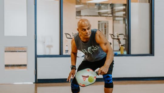 A man winds up for a swing while playing pickleball in a gymnasium.