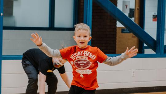 A young boy runs inside a studio space with his arms in the air.