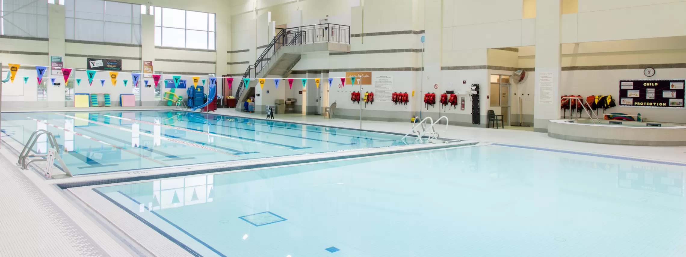 An indoor pool featuring a large pool with a slide and smaller pool with a walk-in.