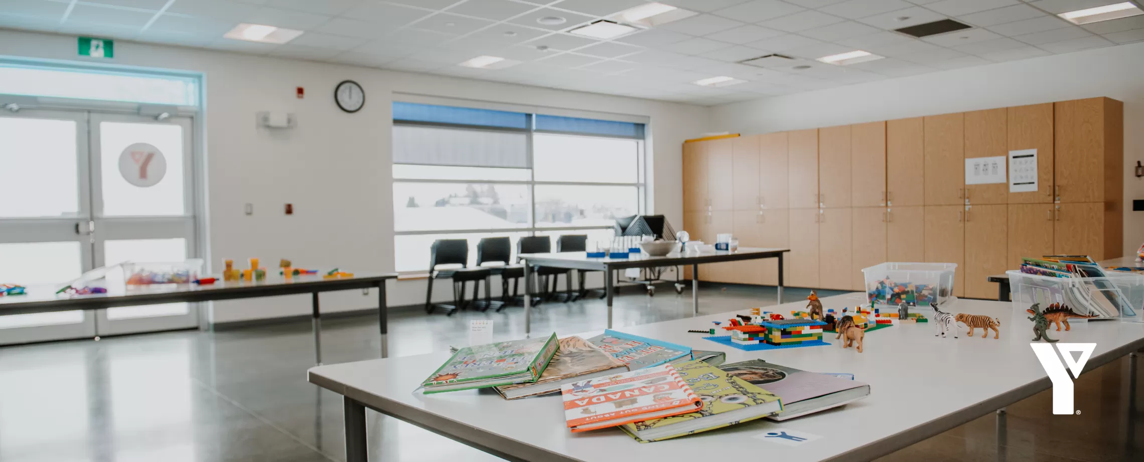 Tables in a sun-filled room are prepared with various children's activities, like books, blocks and science experiments,