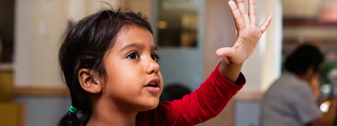 A young girl raisers her hand and asks a question in a YMCA Child Care centre.