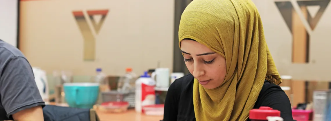 A woman wearing a hijab sits at a table and writes notes during a workshop.