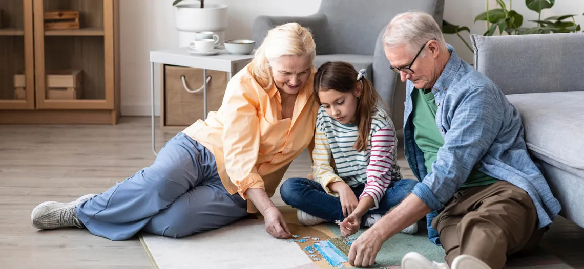 A grandmother, granddaughter and grandfather put a puzzle together on their livingroom floor.