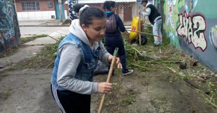 A tennaged girl holds a broom as she cleans an alley with other YMCA program participants.