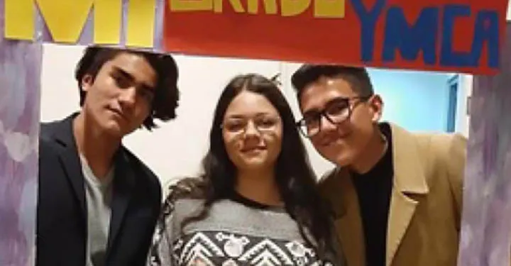 Three teens stand together, holding a sign that says YMCA.