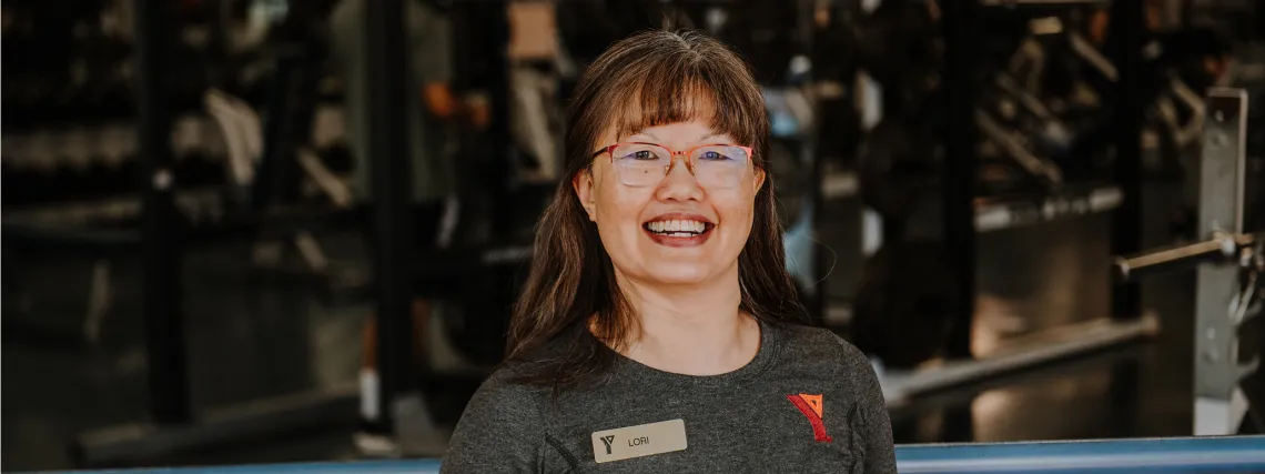 A YMCA staff member wearing glasses smiling for the camera in a fitness centre.