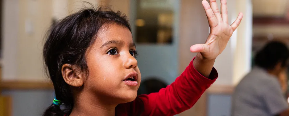 little girl in YMCA child care raising her hand